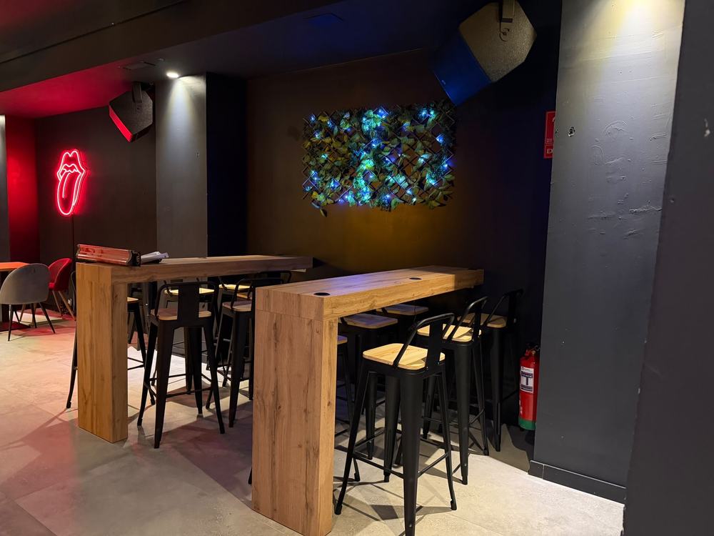 Barras altas con taburetes junto a la pared vegetal iluminada