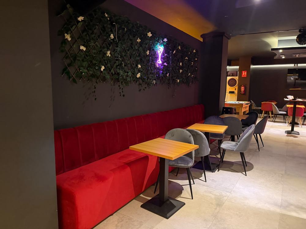 Sofá corrido rojo con mesas bajo la pared vegetal